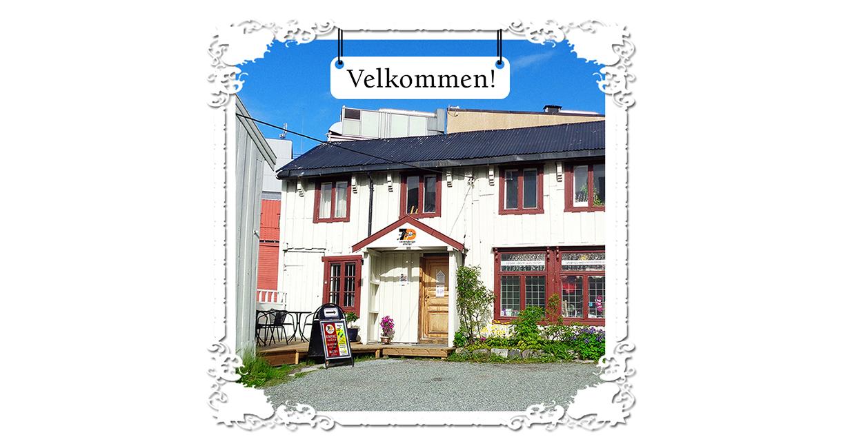 En koselig bygning med rød vinduer og en velkomstskilt, omgitt av en gruslagt gårdsplass.