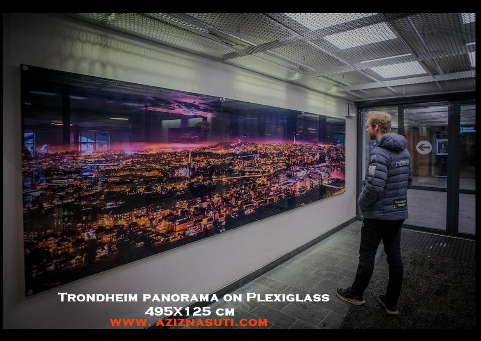 En person ser på et Trondheim panorama trykt på Plexiglass, 495x125 cm, i en moderne innendørs setting.