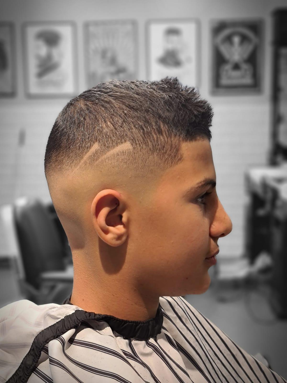 Ung gutt med moderne frisyrer og fade, sitter i frisørsalong med barberstol i bakgrunnen.