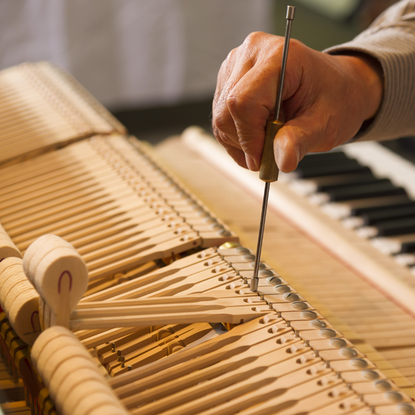 En hånd som justerer en piano mekanisme med et verktøy, med tangenter i bakgrunnen.