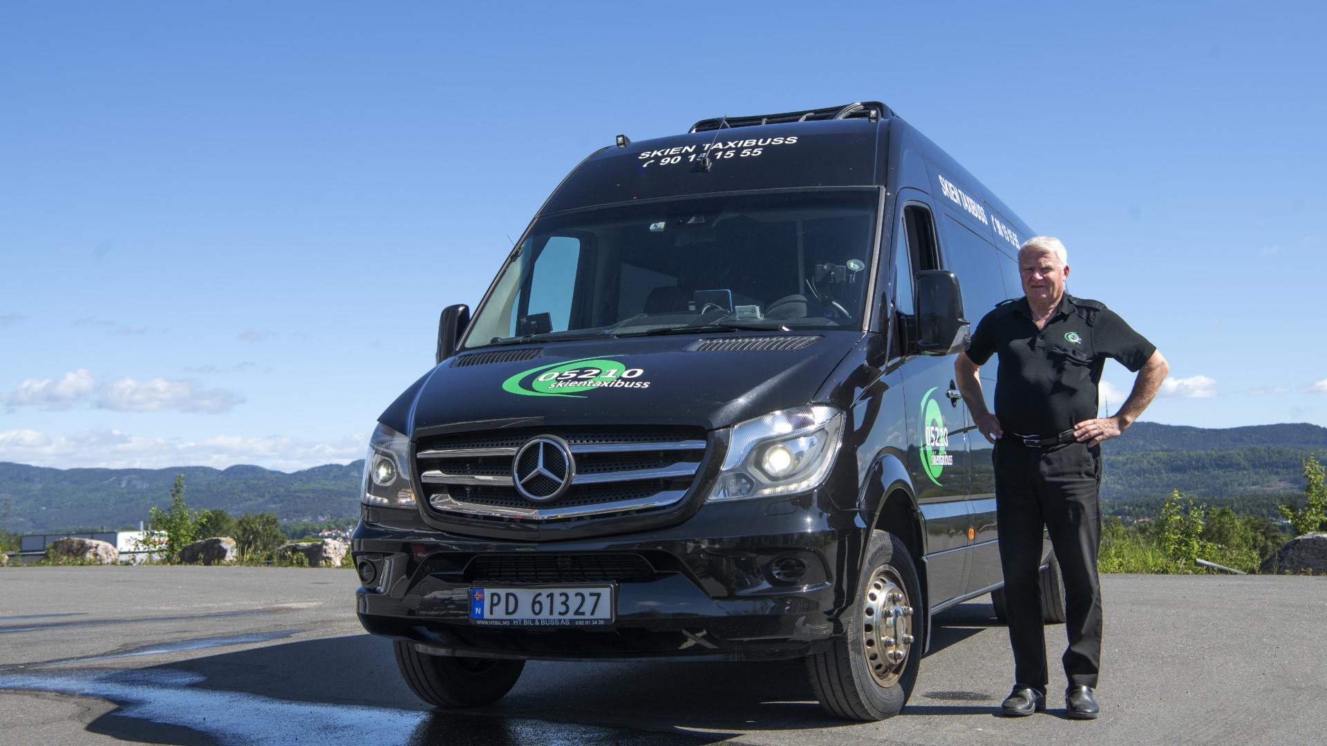 En mann står ved siden av en svart Mercedes varebil med logo, med fjell i bakgrunnen.