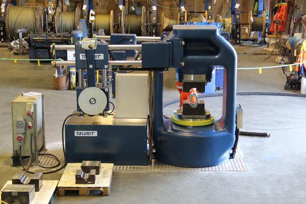 En industriell maskin for bearbeiding av metall, plassert i en verksted med store spoler i bakgrunnen.