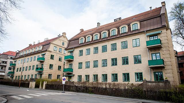 To bygninger med grønne balkonger og vinduer, beliggende ved en gate med fotgjengerovergang.
