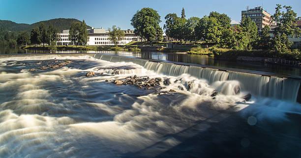 En vakker foss med strykende vann, omgitt av trær og bygninger i bakgrunnen.