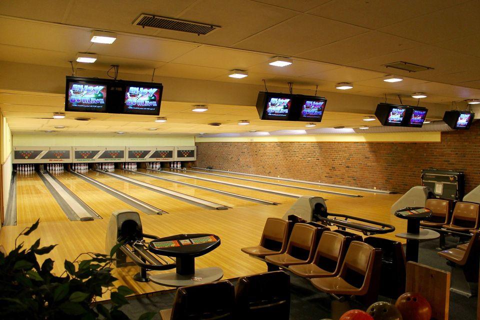 En moderne bowlinghall med flere baner, stoler og skjermer som viser resultater.