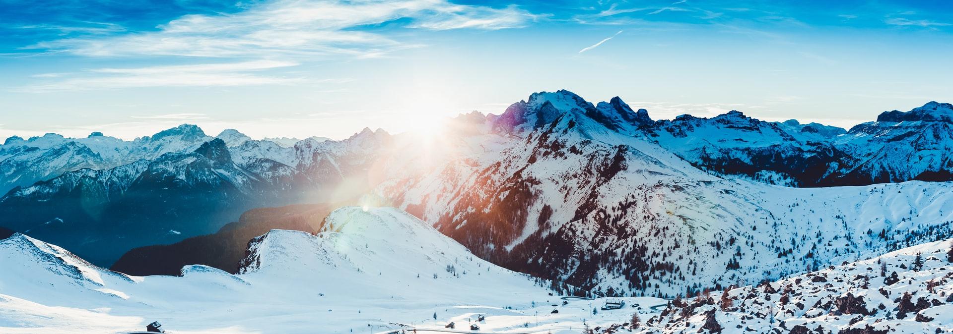 Vinterlandskap med snødekte fjell og soloppgang over horisonten i en klar blå himmel.