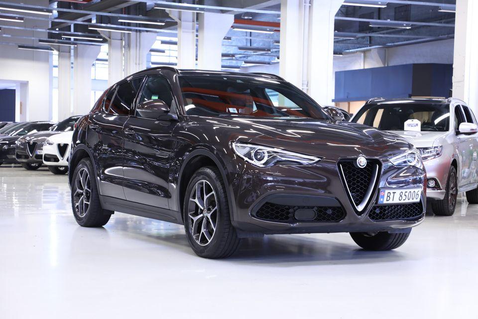 En mørk brun Alfa Romeo Stelvio SUV parkert i en moderne bilutstillingshall.