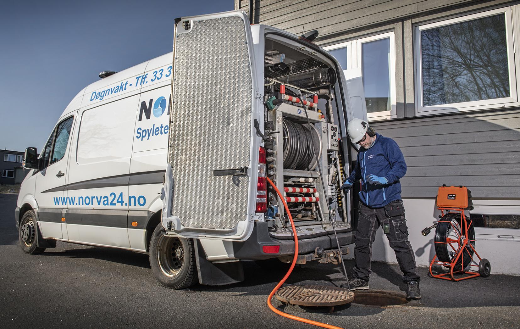 En servicemann jobber med en rørleggerbil, som har utstyr for rørinspeksjon og rensing, ved en bygning.