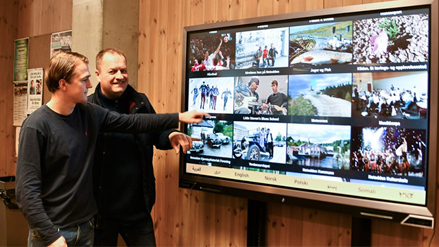 To personer peker på en stor skjerm med bilder fra ulike aktiviteter og arrangementer.
