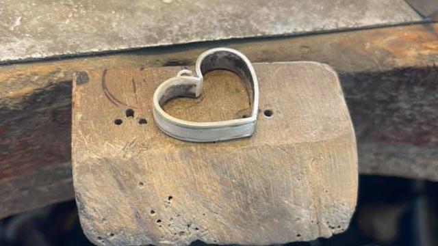 Hjerteformet ring laget av metall, plassert på en treblokk i et verksted.