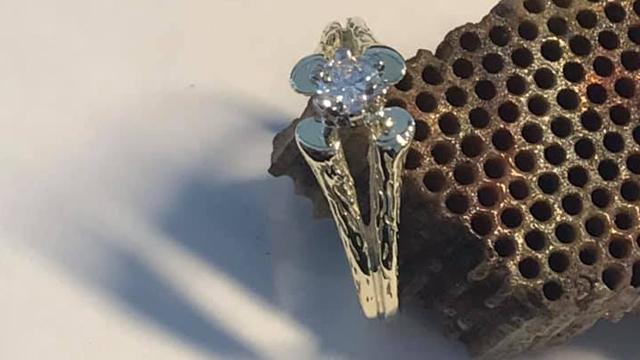 En elegant ring med en stor diamant i midten og tre mindre diamanter på sidene, plassert på en rustikk bakgrunn.