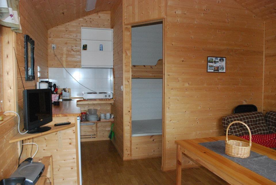 Koselig hytteinnvendig med trevegger, kjøkkenkrok, stue med TV og spisebord, samt sovealkove med køyesenger.