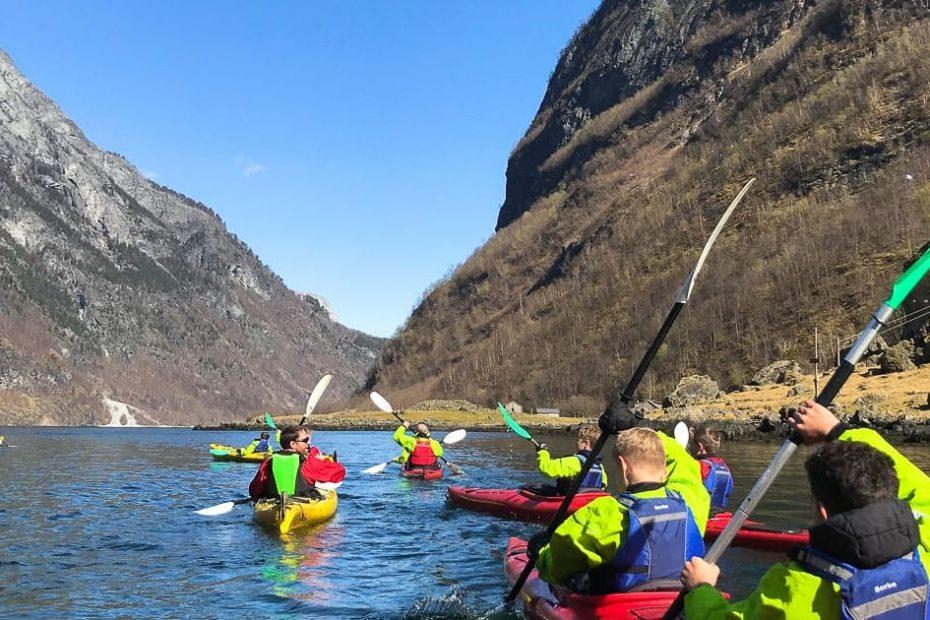 Gruppe med kajakkpadlere i fargerike klær på en innsjø omkranset av fjell. Solfylt dag med klar blå himmel.
