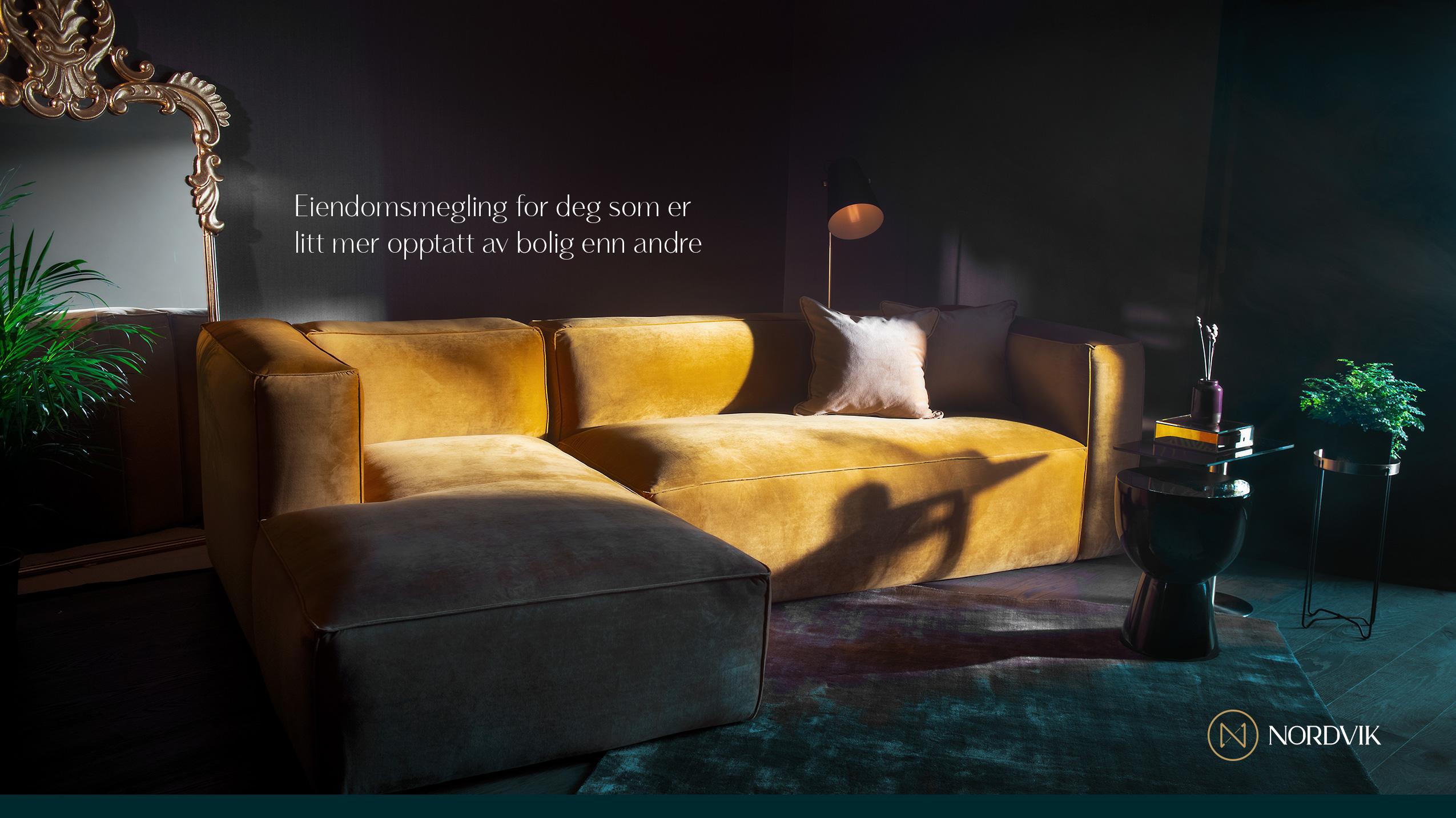 Moderne stue med en gul sofa, stilige planter og en elegant lampe i et mørkt rom.