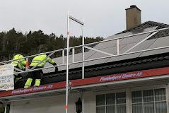 To personer i refleksvester installerer solcellepaneler på taket av et hus.