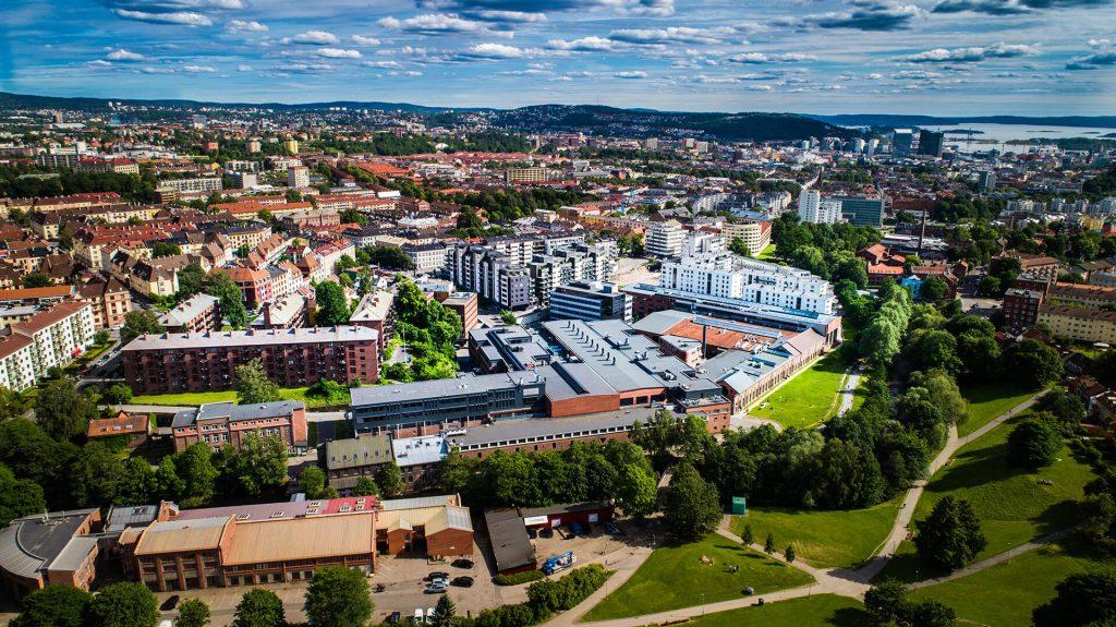 Oversiktsbilde av Oslo med bygninger, parker og himmel dekket av skyer.