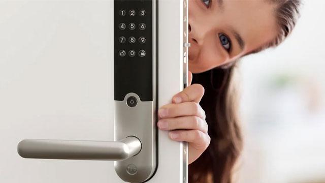 En jente kikker frem fra en dør med et digitalt låsesystem.