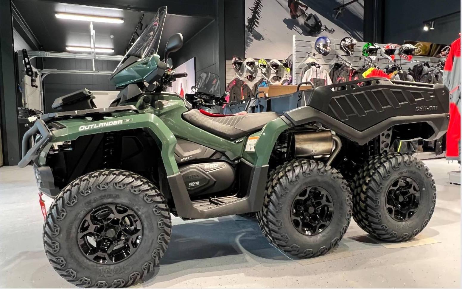 En grønn ATV med seks hjul står i en butikk, omgitt av hjelmer og annet utstyr.