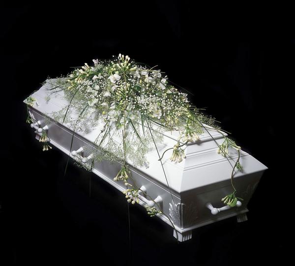 Hvit kiste dekorert med blomster og grønt, plassert på en svart bakgrunn.