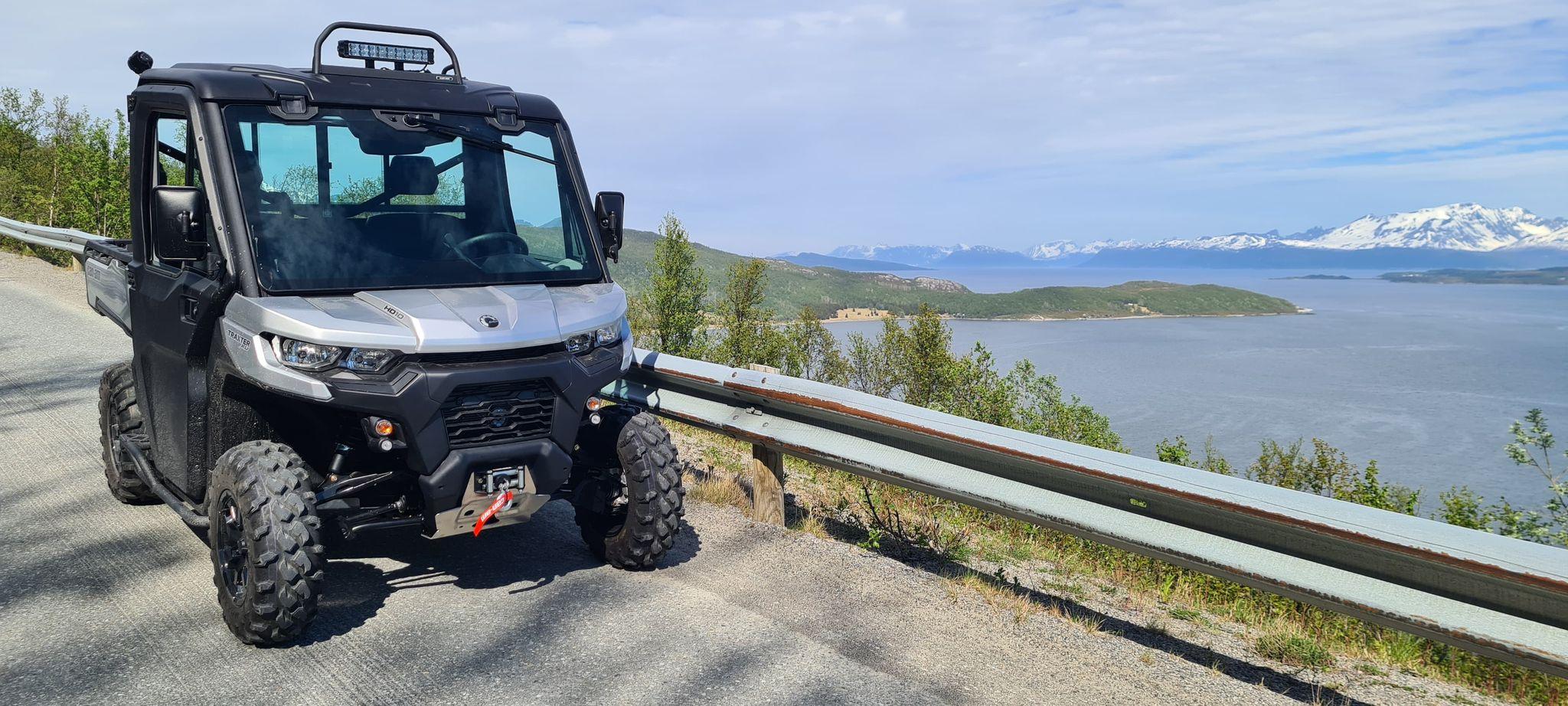 En svart ATV parkert langs en vei med utsikt over fjorden og fjellene i bakgrunnen.