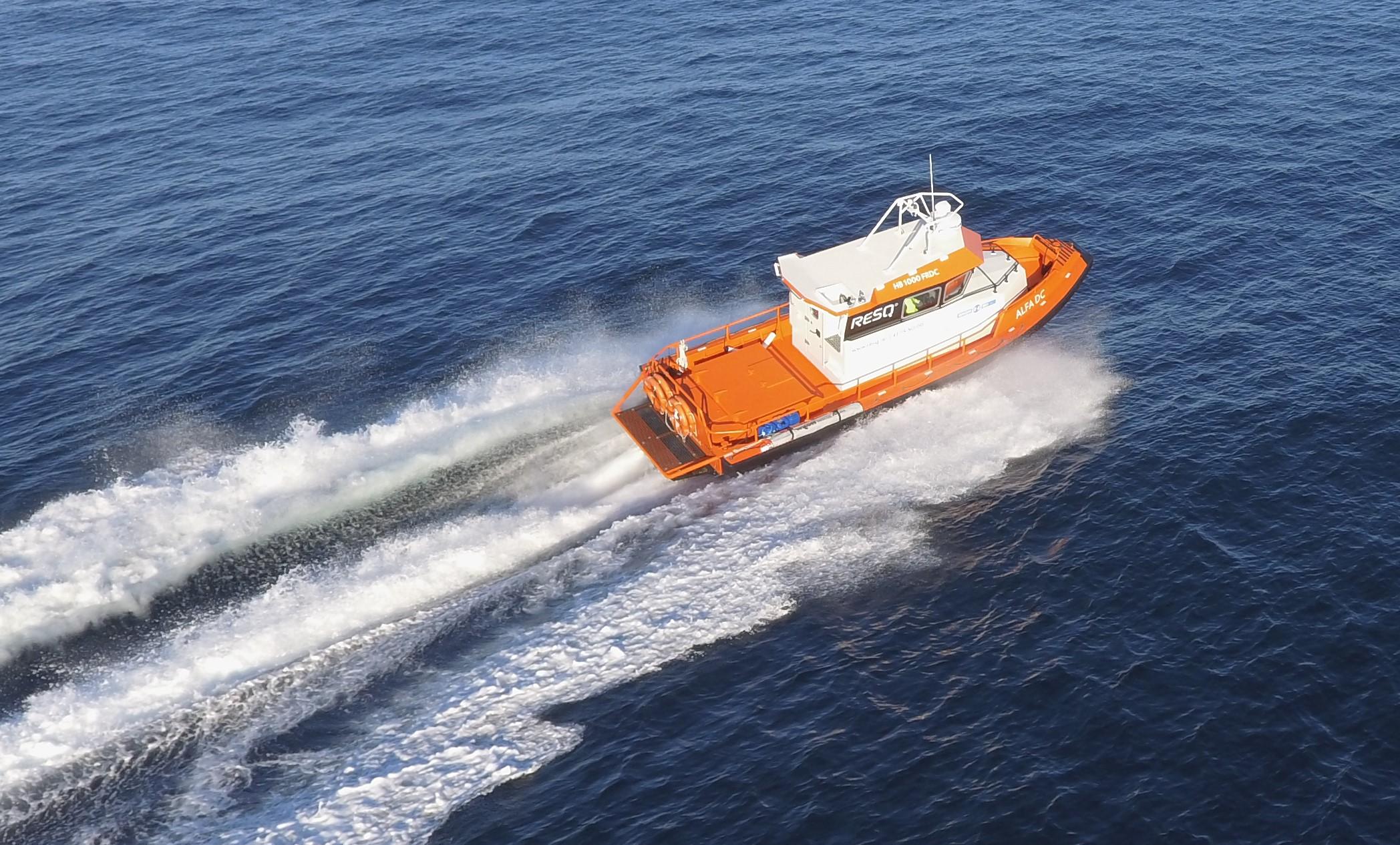 En oransje båt som kjører raskt over havet med bølger bak seg.