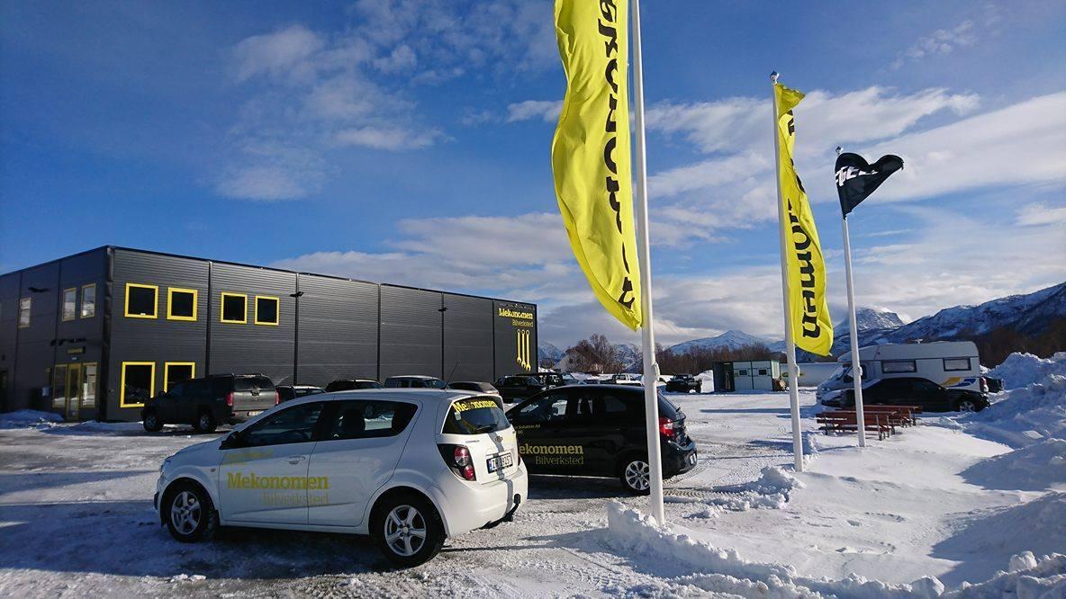 En bil med logoen til et bilutleiefirma står parkert foran en moderne bygning med gule detaljer og flagg i snøen.