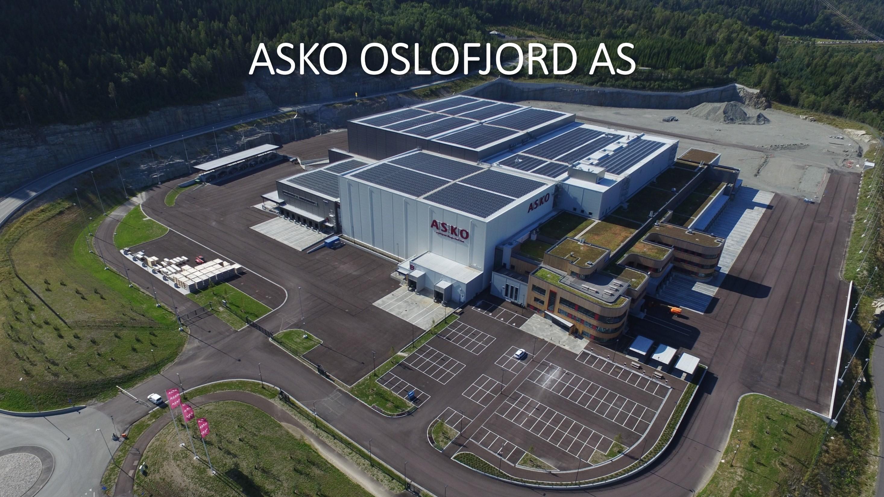 Moderne ASKO Oslfjord AS lagerbygning med solcellepaneler og parkeringsplasser i naturskjønt område.