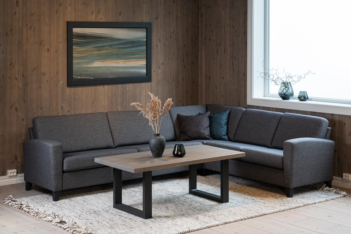 Moderne stue med grå sofaer, et trekaffebord og en maleri på veggen. Vaser med planter på vindusbrettet.
