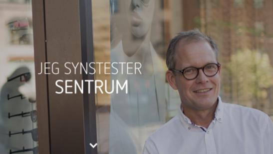 En smilende mann med briller står foran en butikkvindu med tekst som sier "Jeg syns tester sentrum".