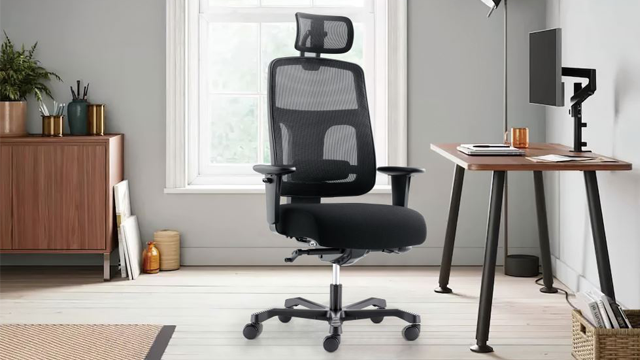 Moderne kontorstol med nettmateriale, plassert ved et skrivebord i et lyst rom med vindu.