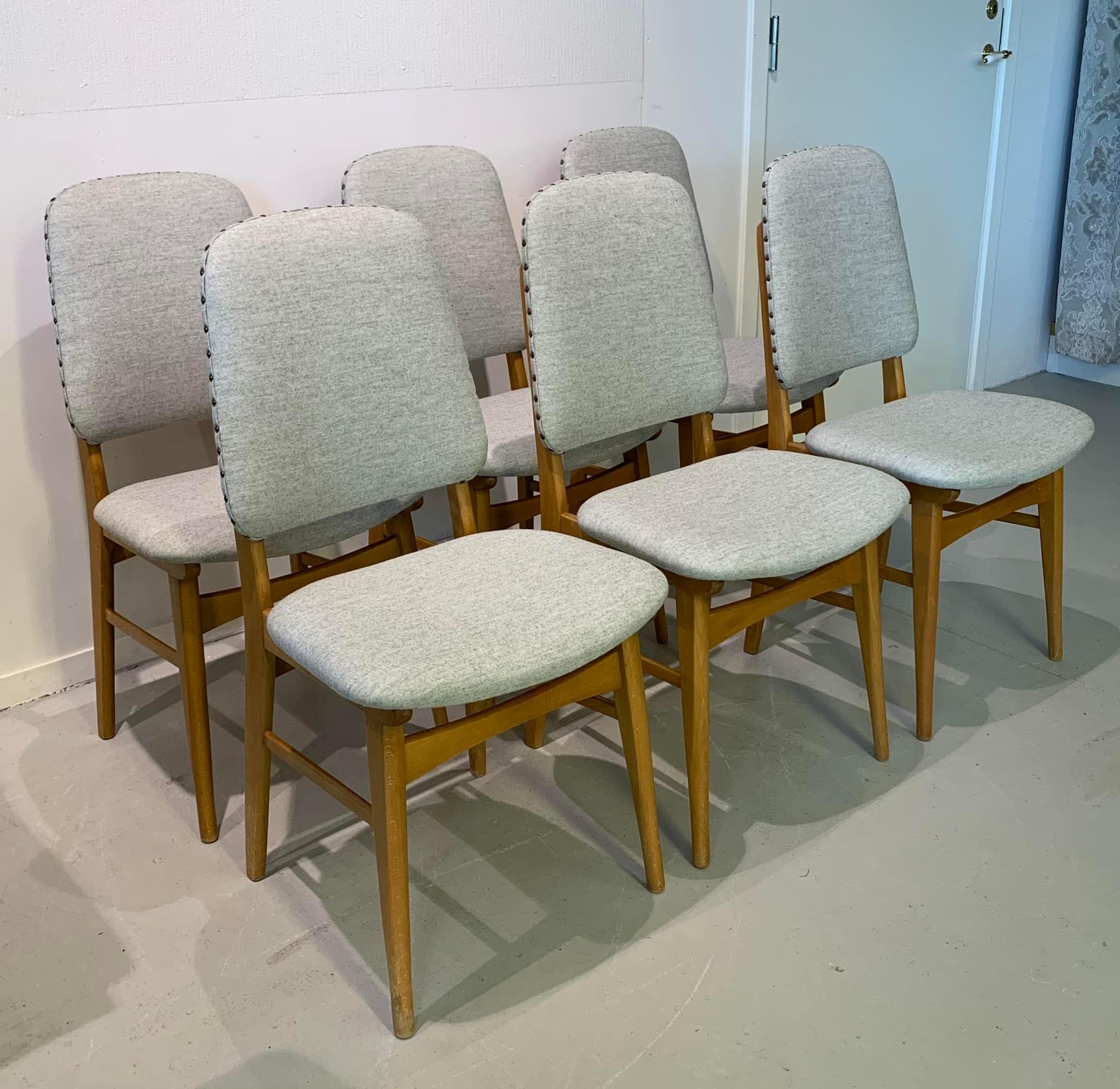 Seks grå stoler med treben, plassert på et lyst gulv i et rom.