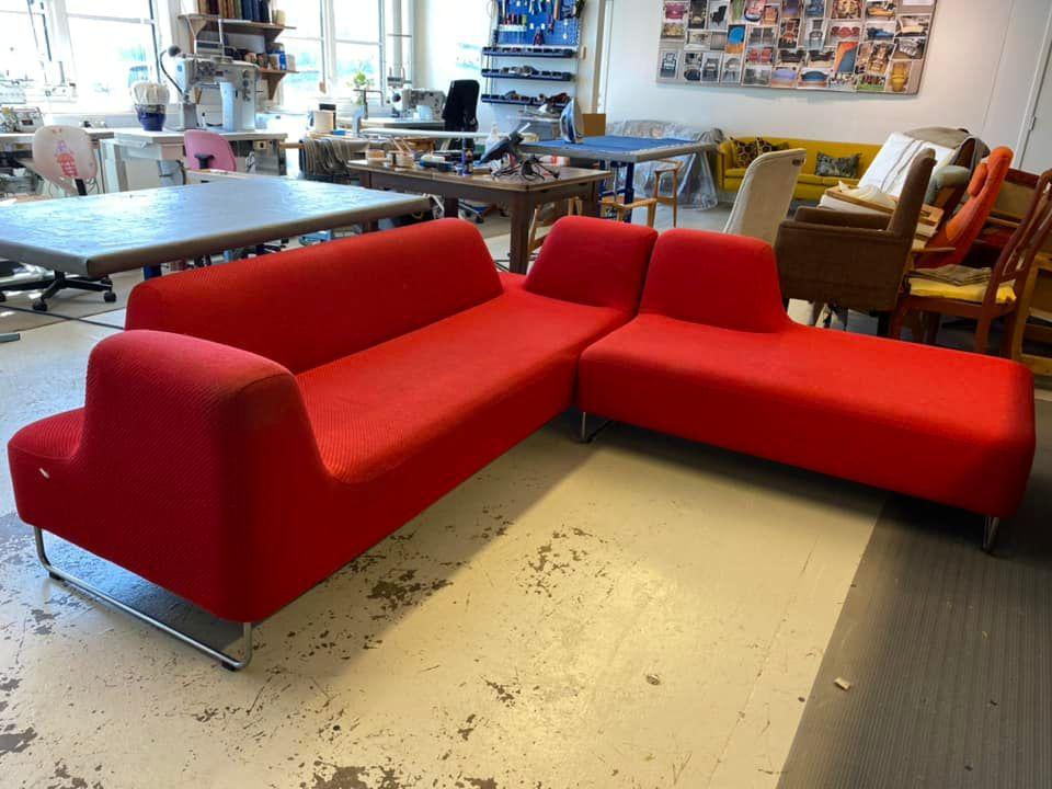 Rød sofa med moderne design, plassert i et rom med flere møbler og kunstverk på veggen.