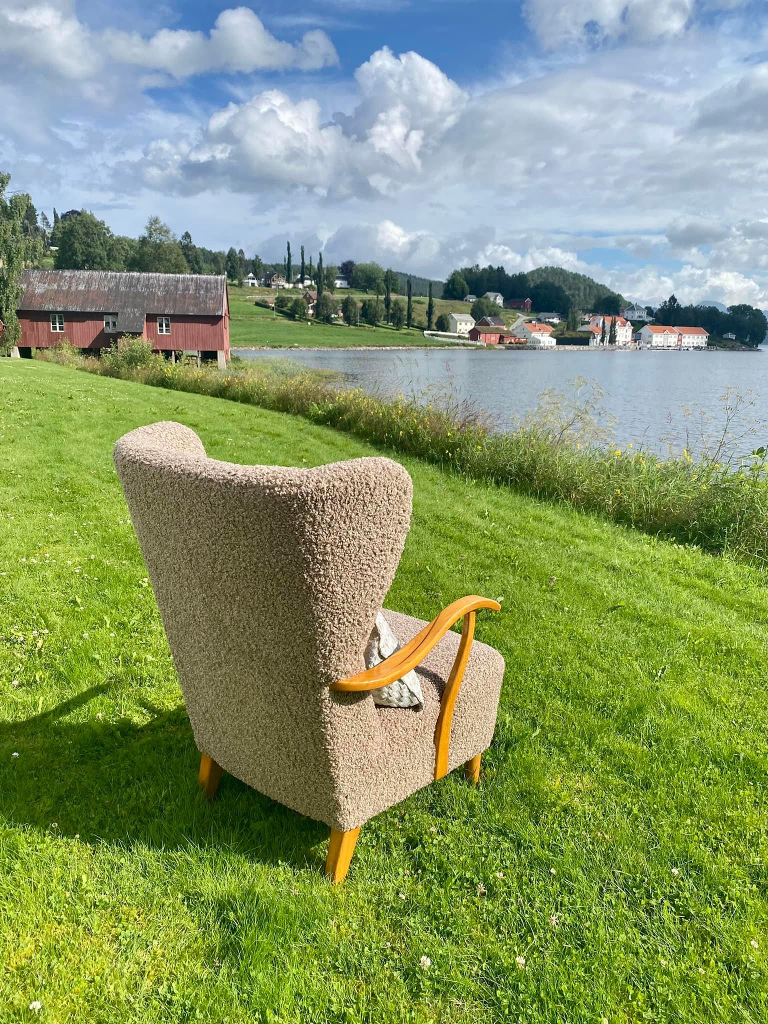En komfortabel lenestol står på gresset med utsikt over en innsjø og bygninger i bakgrunnen.