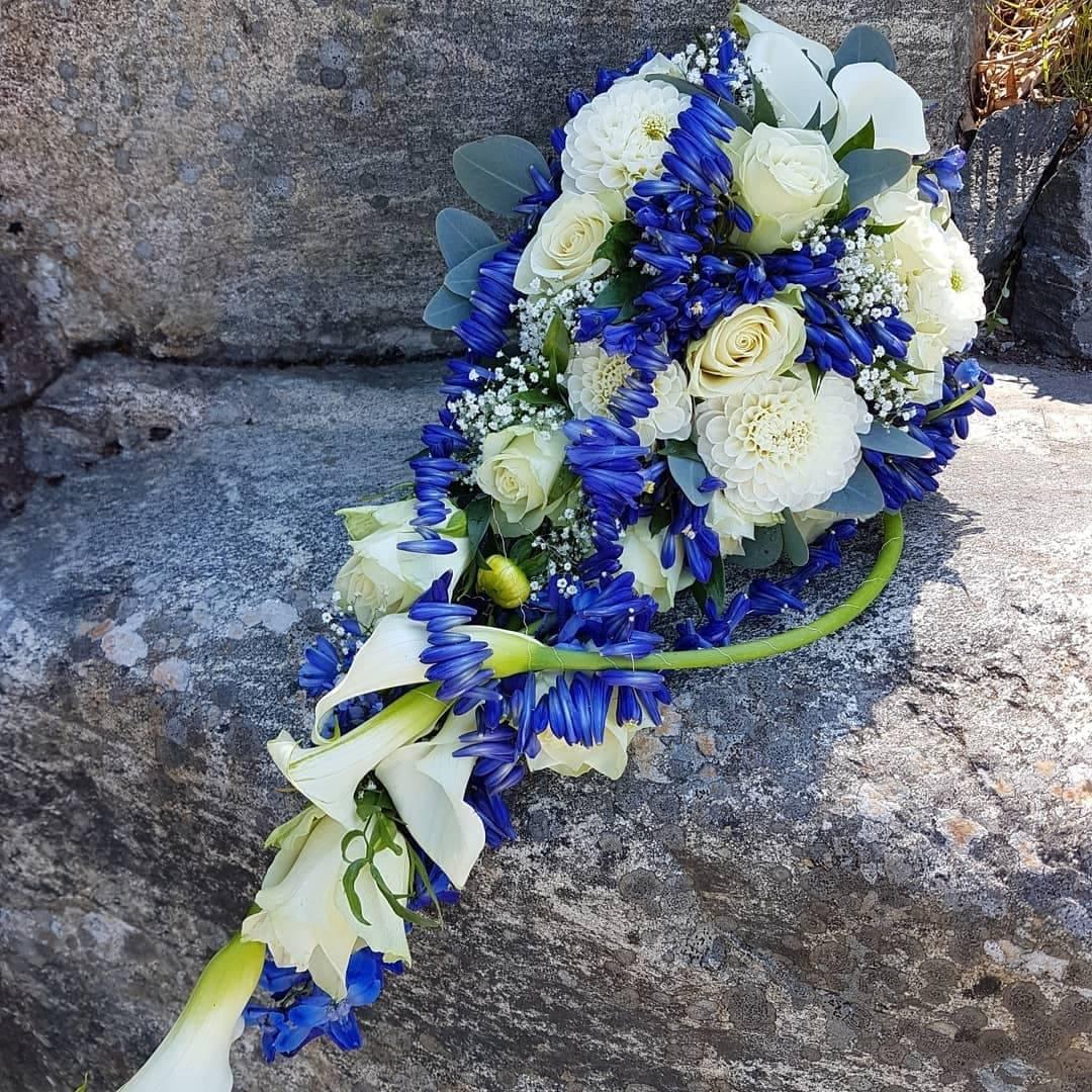 En vakker brudebukett med hvite roser, blåklokker og grønt, plassert på en stein.