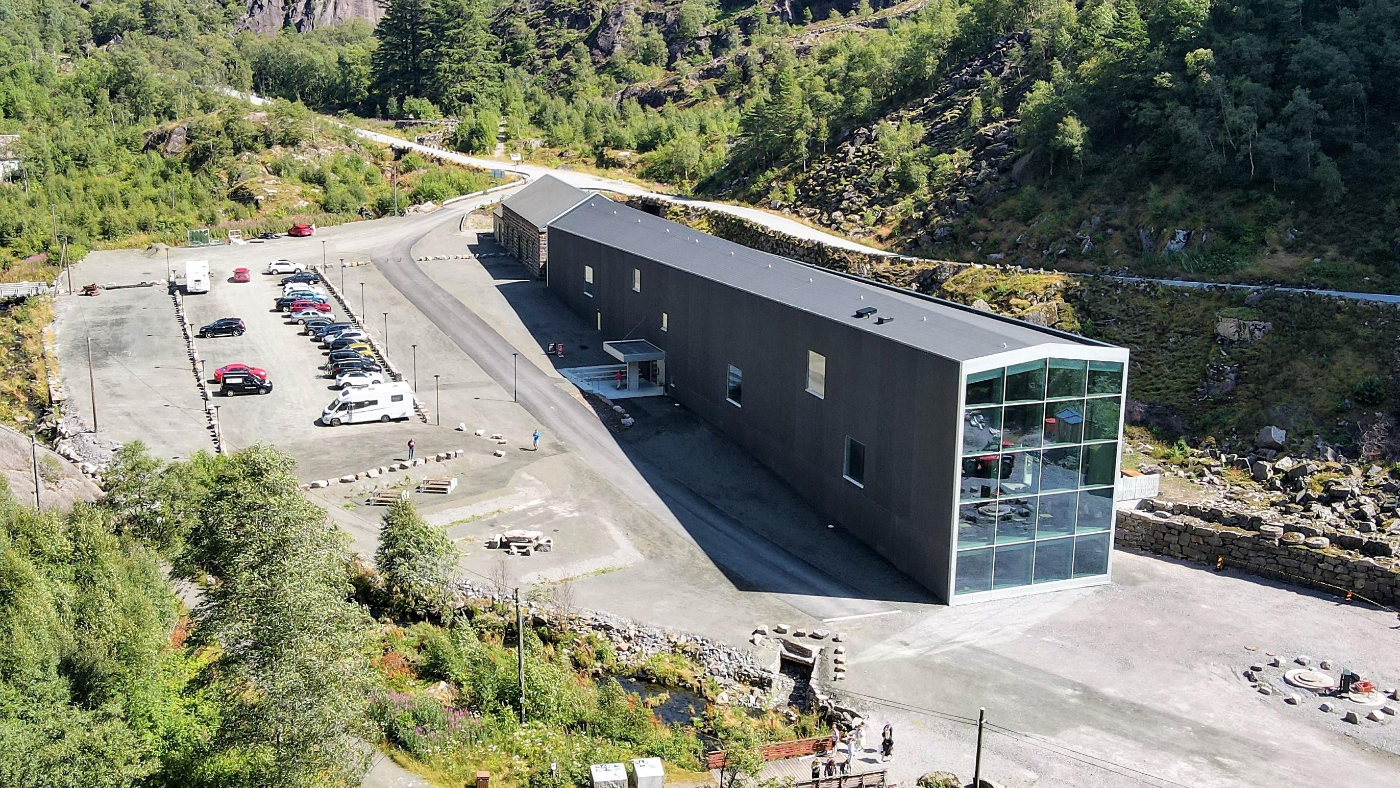Moderne bygning med glassfasade og parkeringsplass omgitt av grønn natur i Norge.