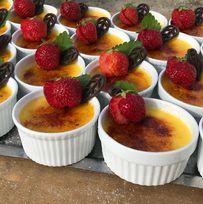 Kremet crème brûlée i små hvite skåler, toppet med friske jordbær og sjokoladebiter.