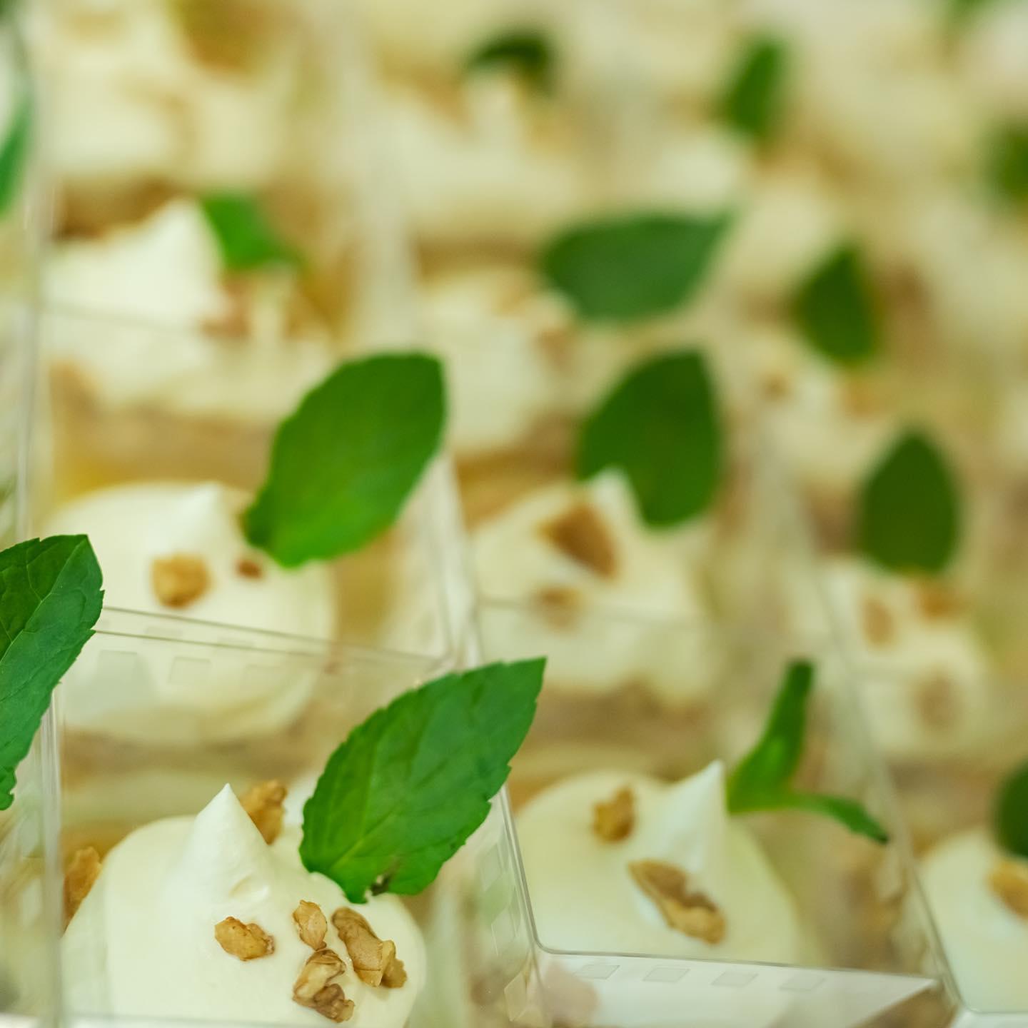 Kremete dessertkopper med mynteblader og nøttebiter, servert i gjennomsiktige beholdere.