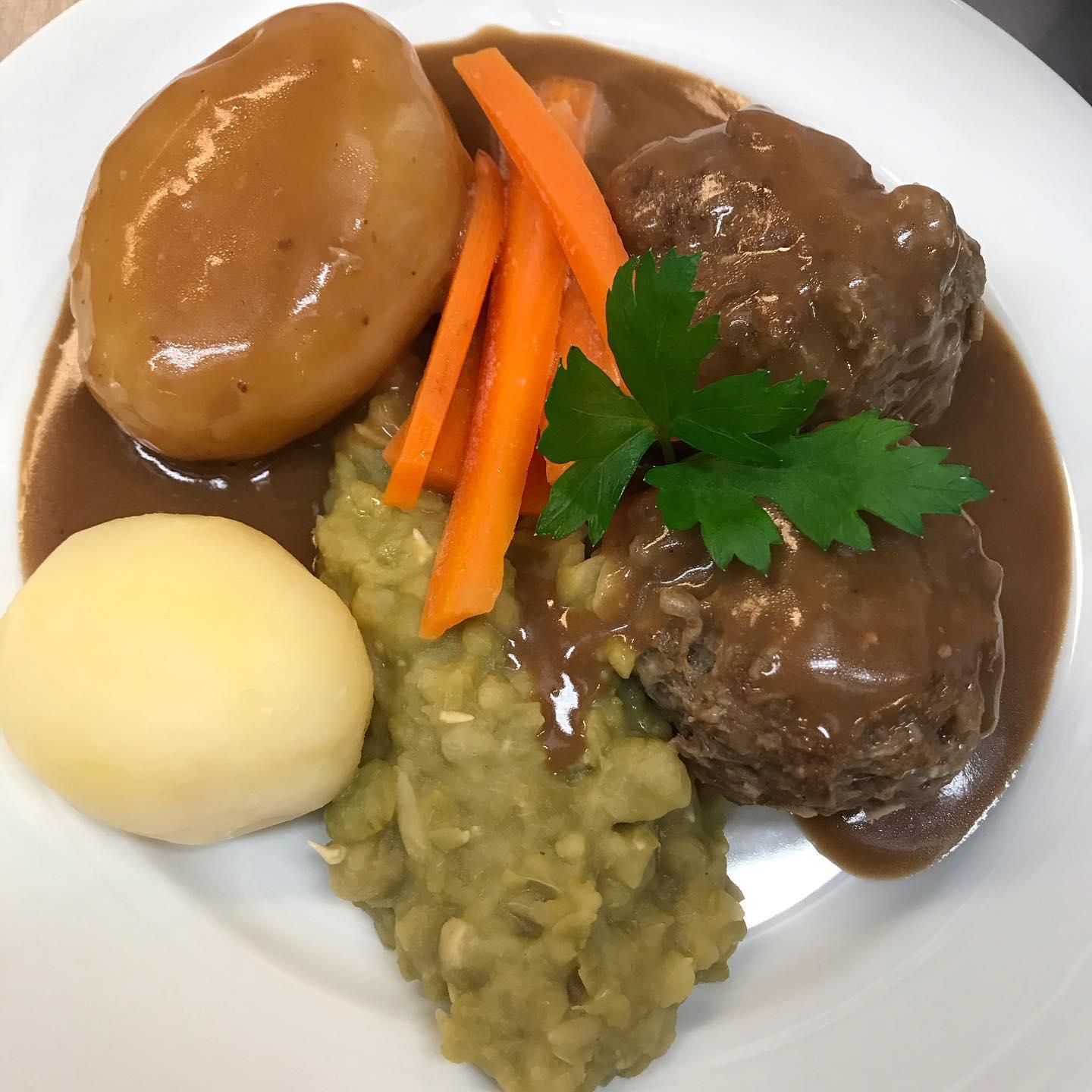 Kjøttkaker med brun saus, poteter, gulrøtter og ertestuing på en hvit tallerken.