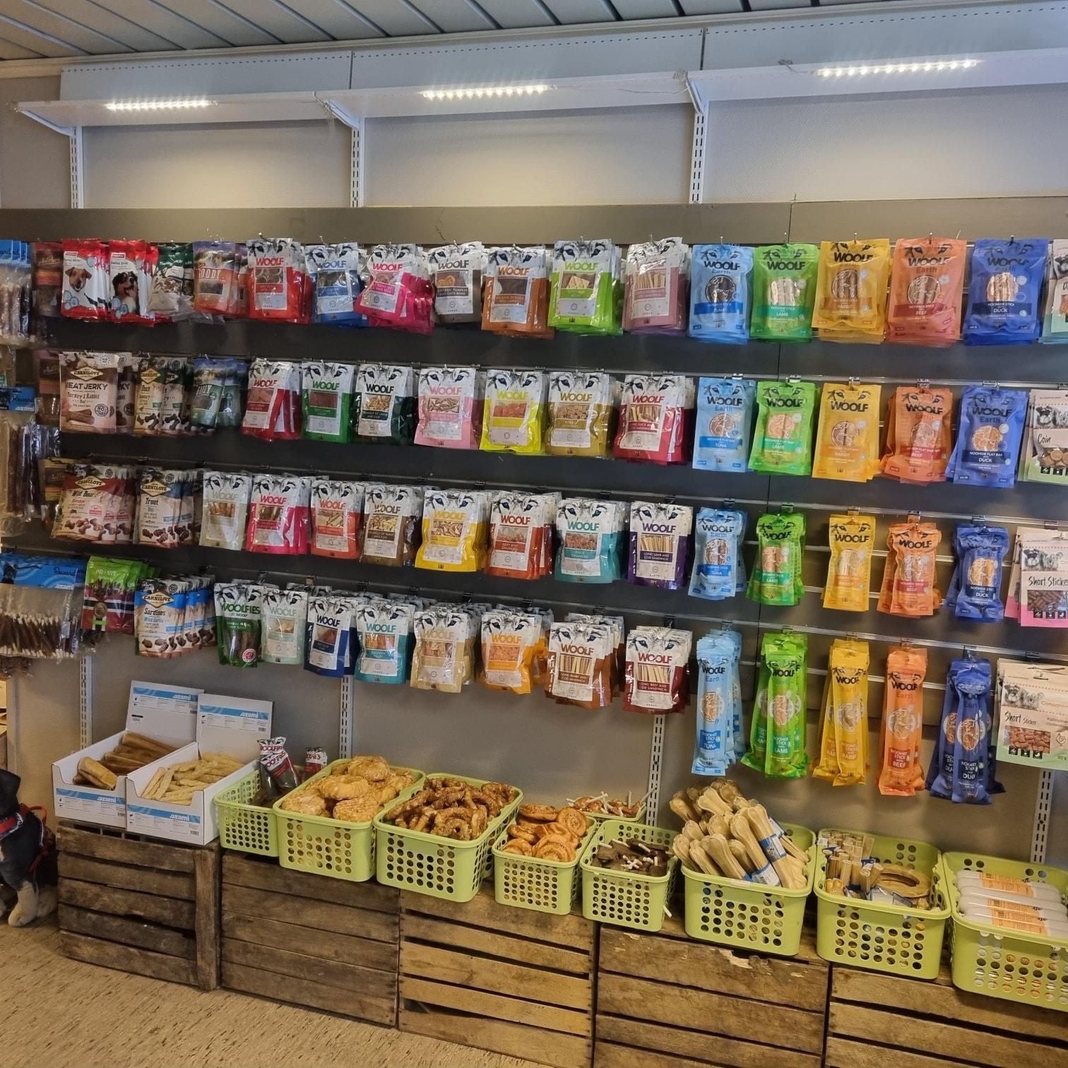 En butikkvegg med hyller fylt med forskjellige hundegodteri og snacks i fargerike pakker.