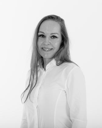 Kvinne med langt hår iført hvit skjorte, smilende mot kameraet på en lys bakgrunn.