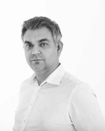 Portrett av en mann med grått hår, iført hvit skjorte, som ser direkte inn i kameraet.