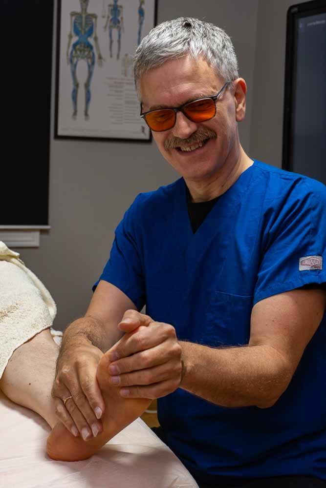En lege i blått arbeidstøy masserer en pasients fot i et behandlingsrom.