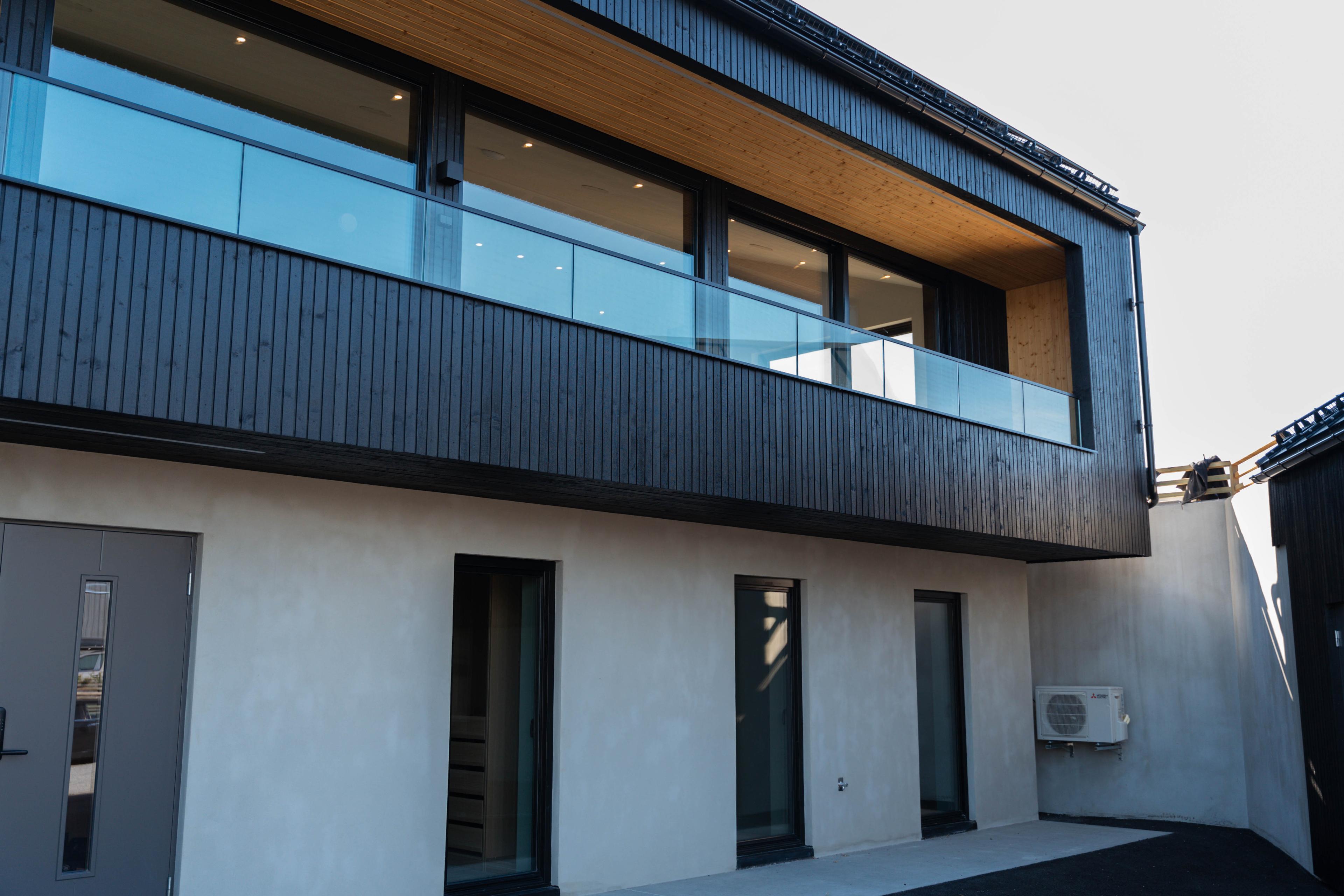 Moderne bygning med svart trepanel, glassbalkong og klimaanlegg på fasaden.