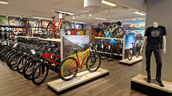 En sykkelbutikk med mange sykler utstilt, inkludert mountainbikes og barnevennlige modeller, samt mannequiner med klær.