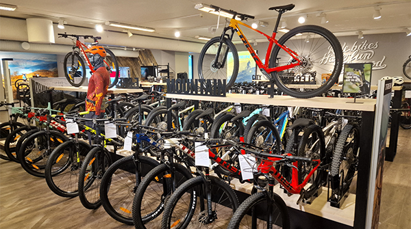 Sykkelbutikk med flere mountainbikes utstilt på hyller og gulv, inkludert fargerike modeller og tilbehør.