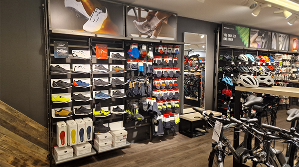 Butikkinnredning med sko, klær og sykkelutstyr på hyller i en sportsbutikk.