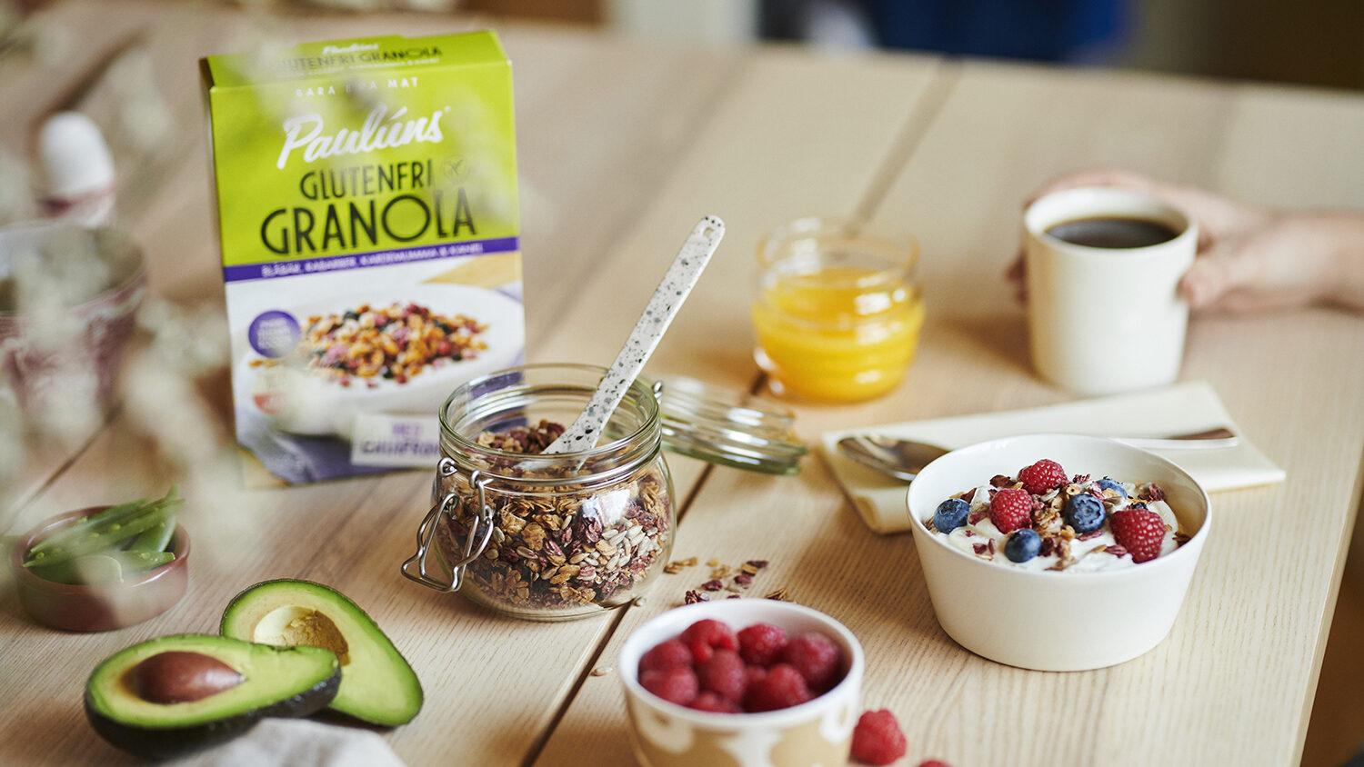 Frokostbord med glutenfri granola, bær, avokado, juice og kaffe i en koselig setting.