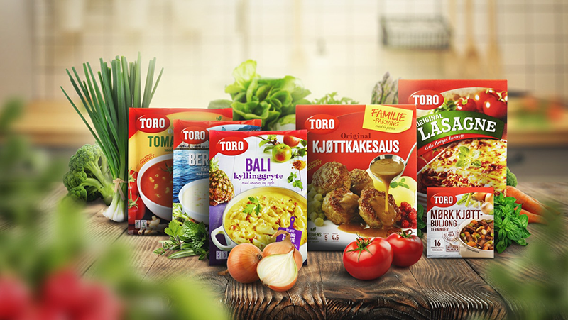 Fargerike Toro matprodukter som tomatsuppe, kjøttkakessaus og lasagne, med grønnsaker i bakgrunnen.