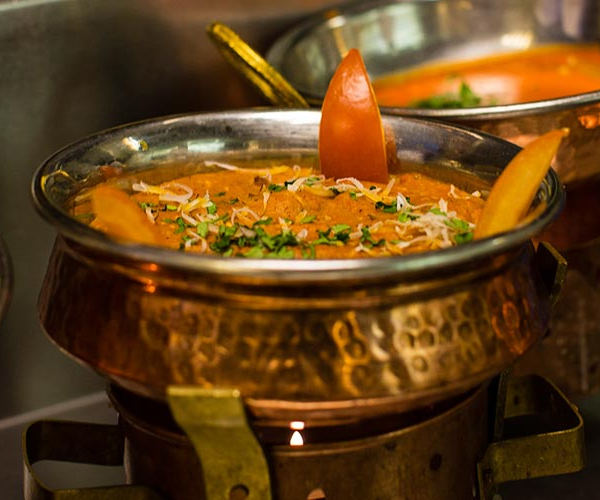 Krydret indisk curry servert i en kobbergryte med tomater og urter på toppen.
