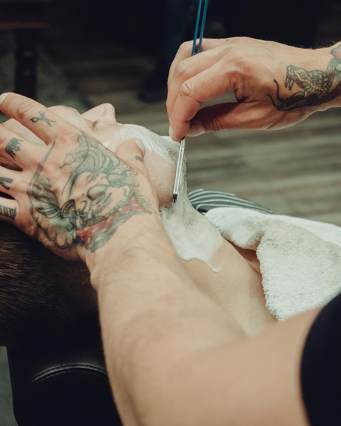 En barberer gir en klassisk barbering med barberkniv til en kunde i en barbersalong.